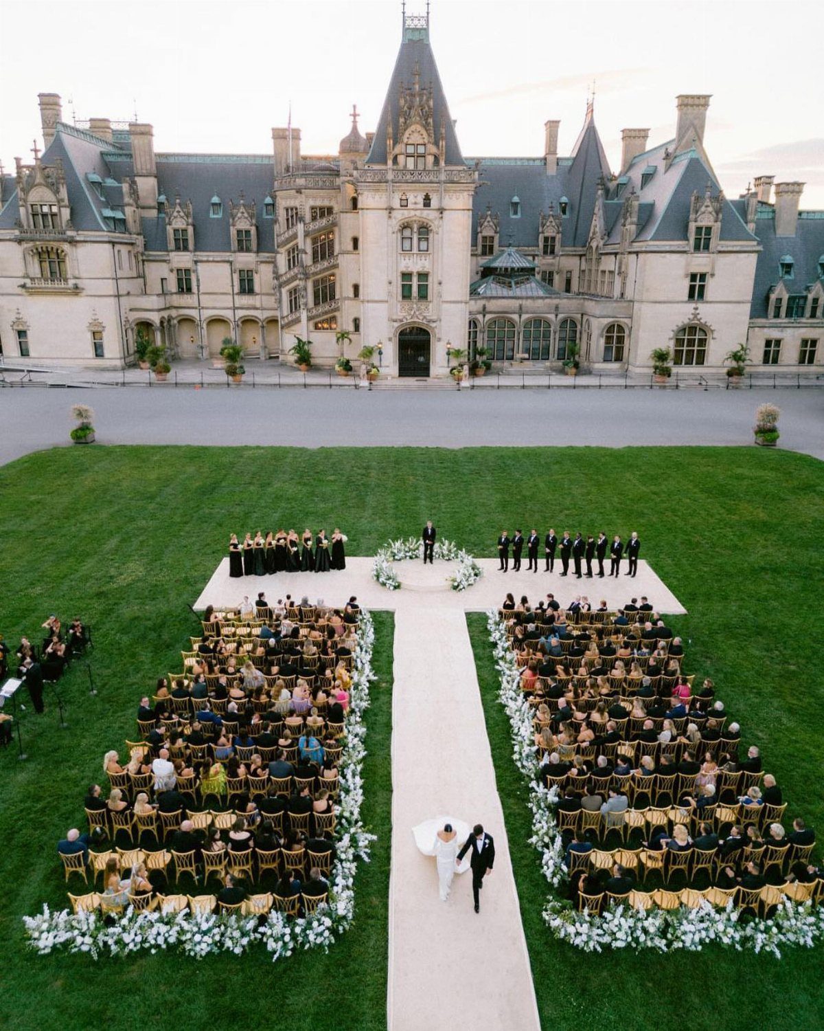 Wedding ceremony on a green lawn in front of the Biltmore Estate castle.
