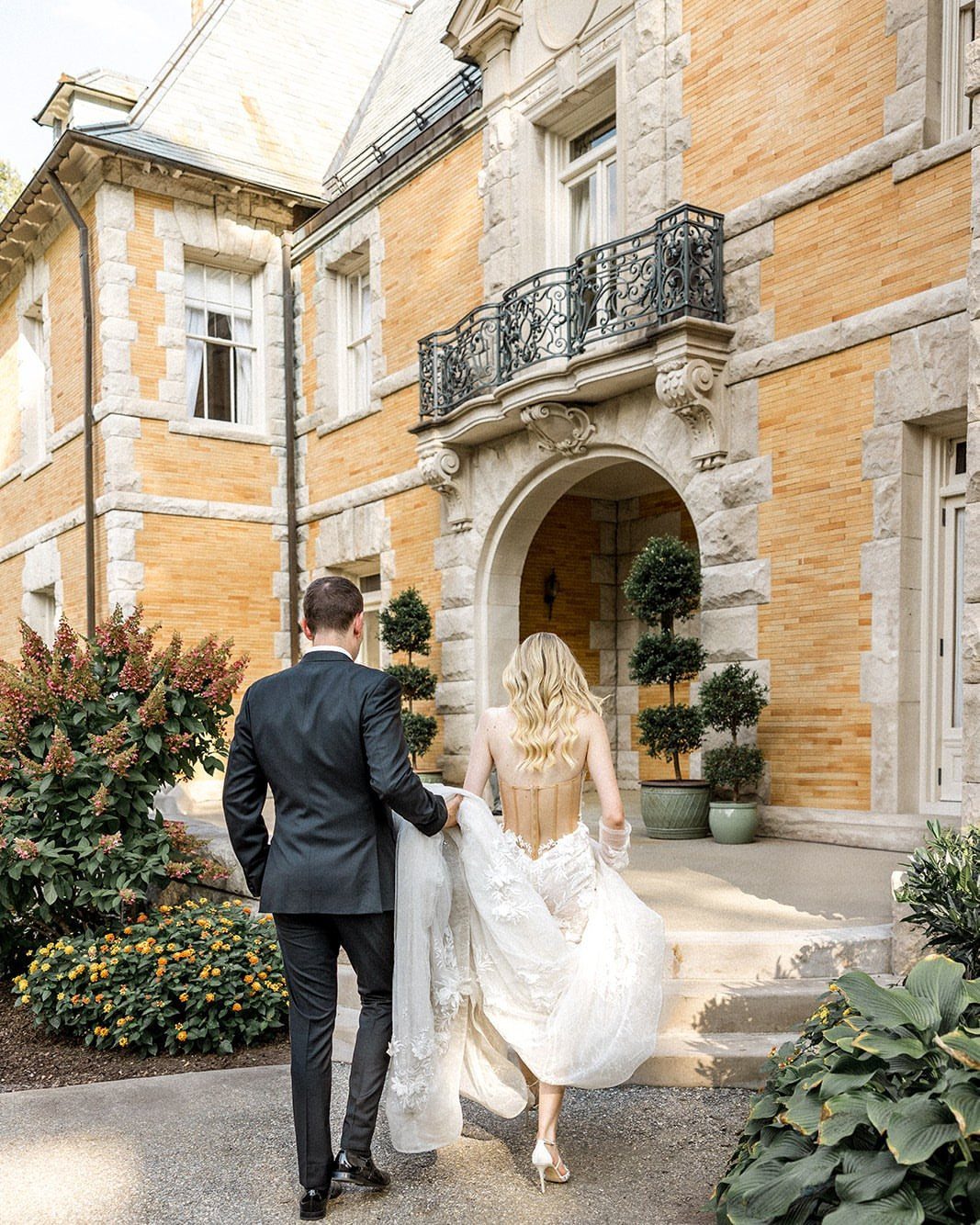 Bride and groom walking toward the arched entrance of a majestic stone French chateau.
