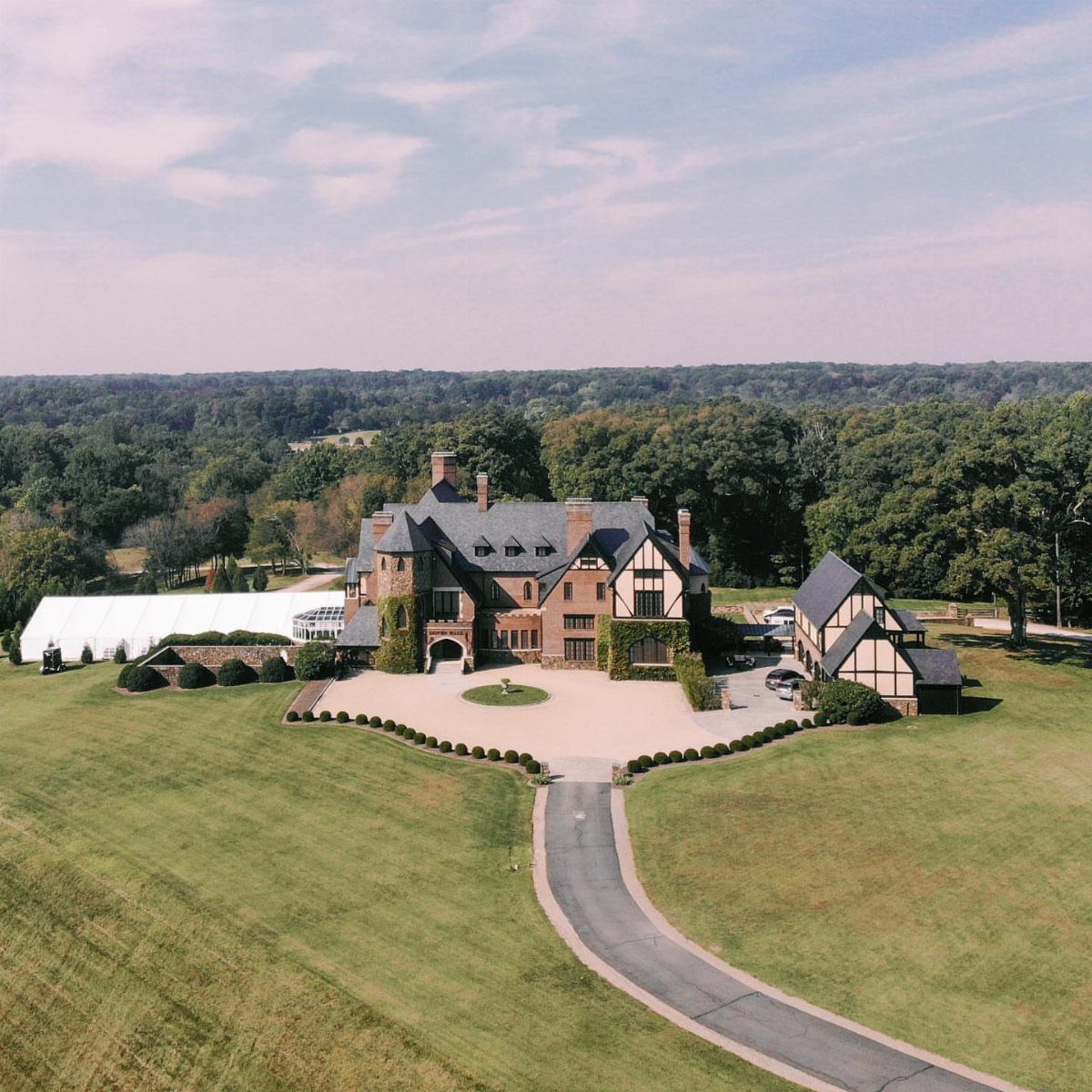 Grand English-style manor house with a white event tent on a green lawn.