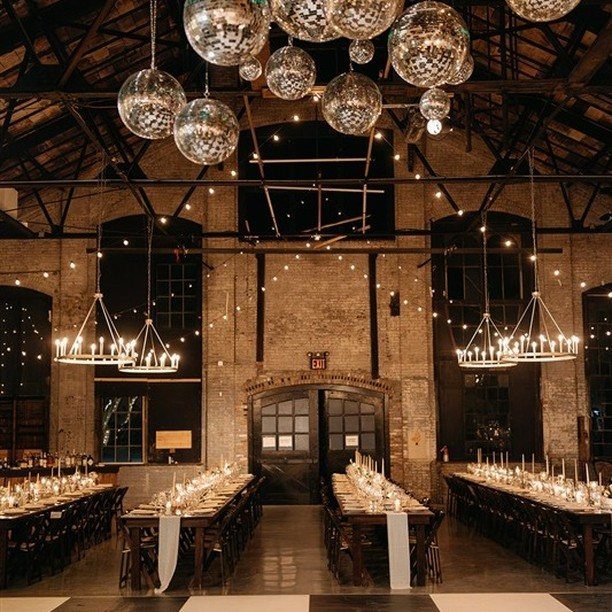 Industrial wedding reception space with disco balls, chandeliers, and long candlelit dining tables.
