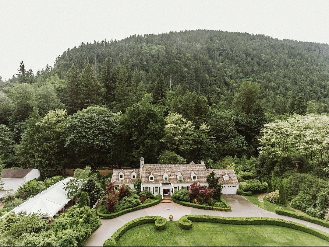 White countryside house with manicured lawns and forests on a large green hill.