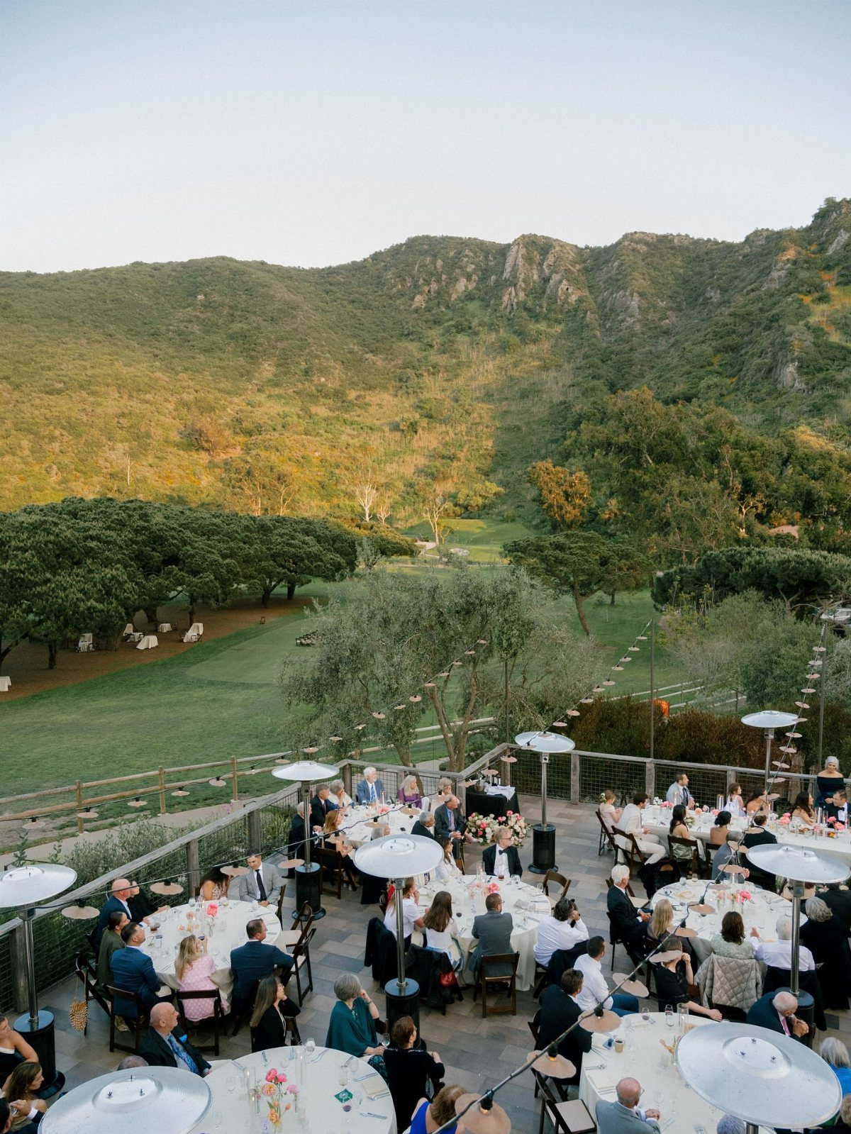 Outdoor wedding reception on a terrace overlooking a green valley and rolling hills.