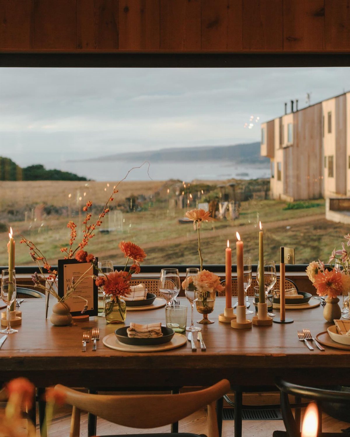 Set dining table with orange flowers and candles overlooking a coastal ocean view.