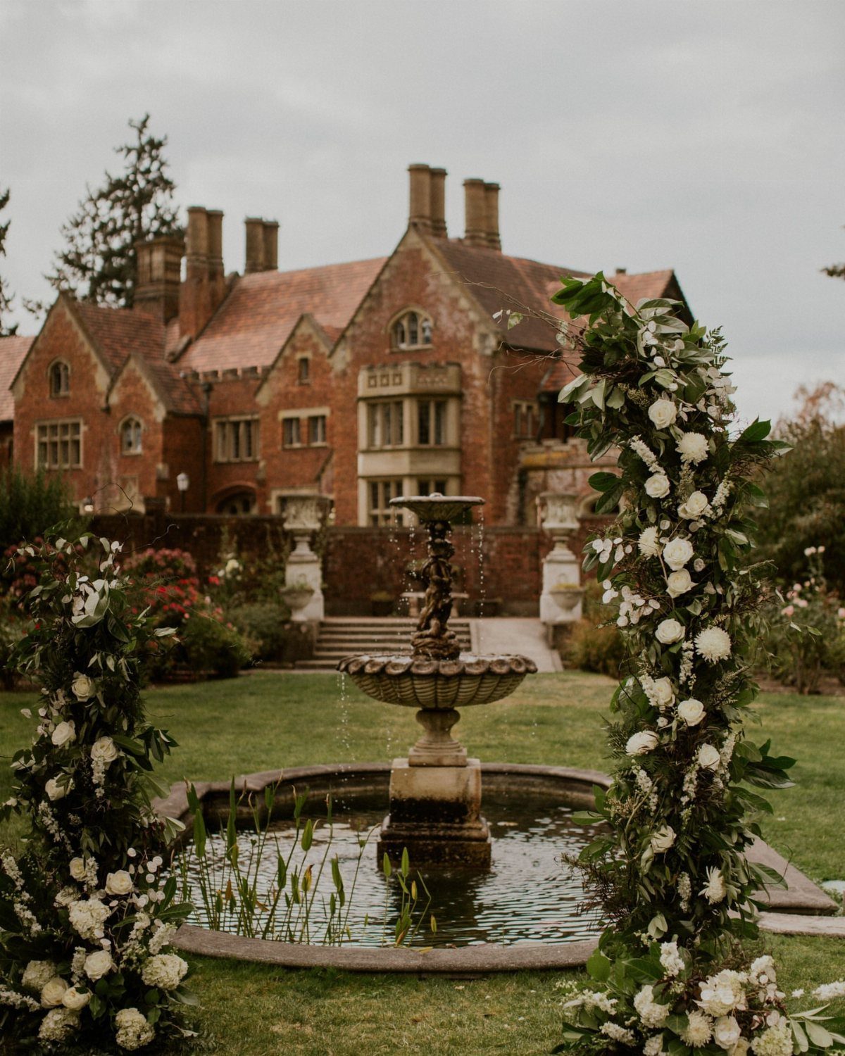 Tudor style brick castle with a tiered stone fountain and white floral arrangements.