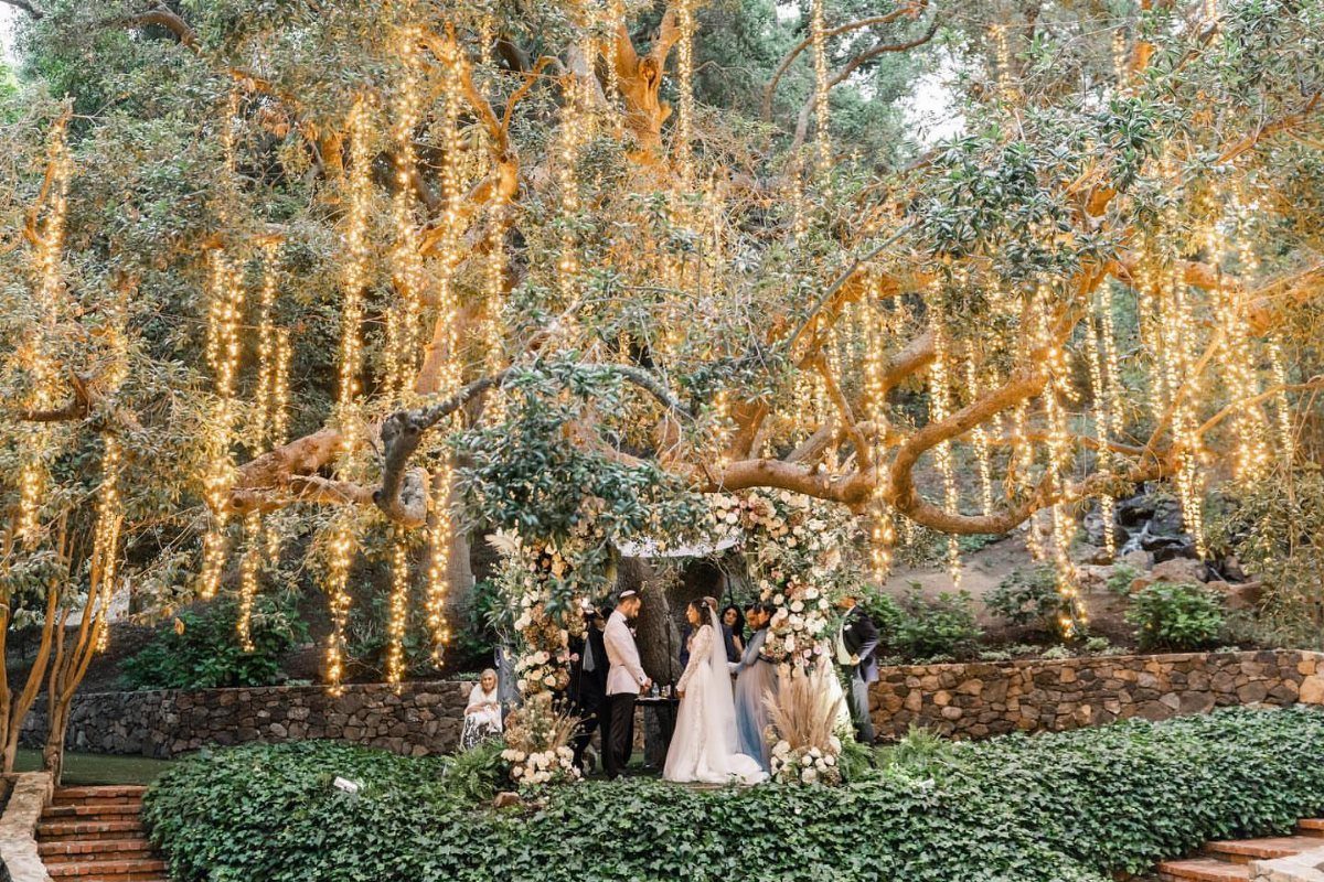 Wedding ceremony under a large tree with hanging fairy lights and floral altar