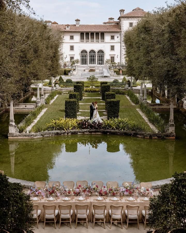 Bride and groom in a formal garden before a grand white historic villa.