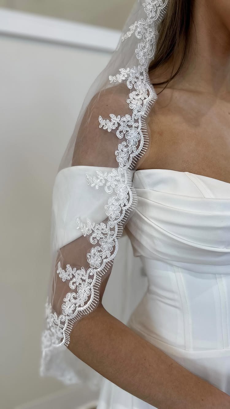 Bride wearing a white off-the-shoulder gown with a lace-edged mantilla veil.