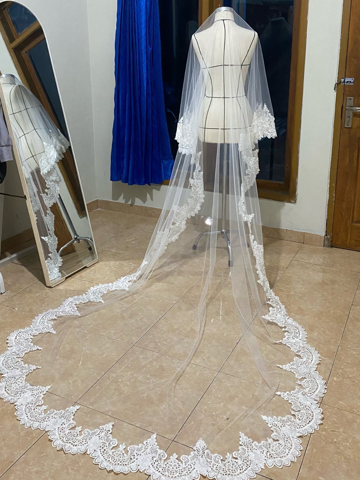 Long white cathedral mantilla veil with lace trim draped on a dress form.
