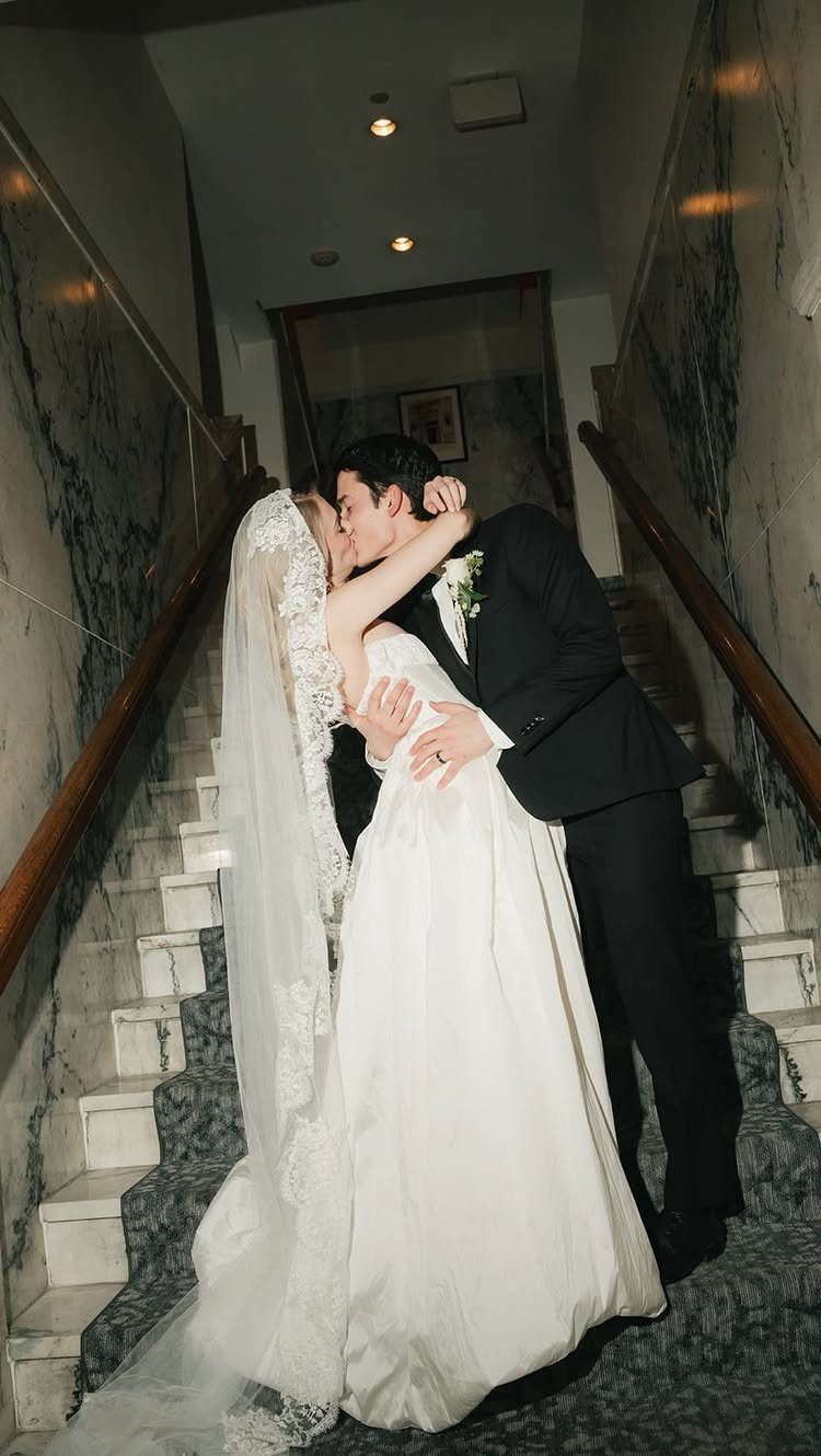 Bride wearing a lace mantilla veil kissing groom on a marble staircase.