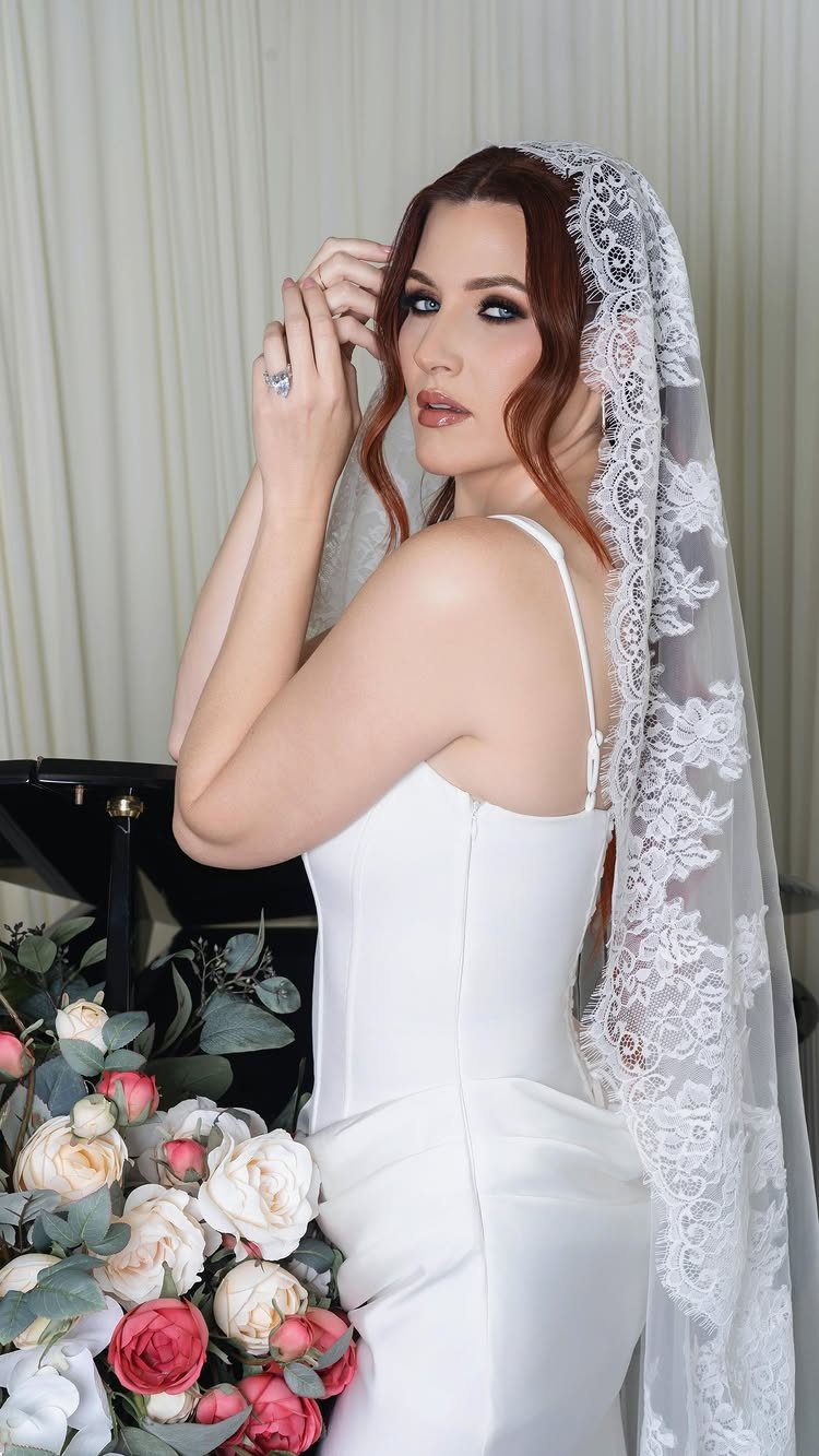 Woman in white bridal gown wearing a long lace mantilla veil with roses.