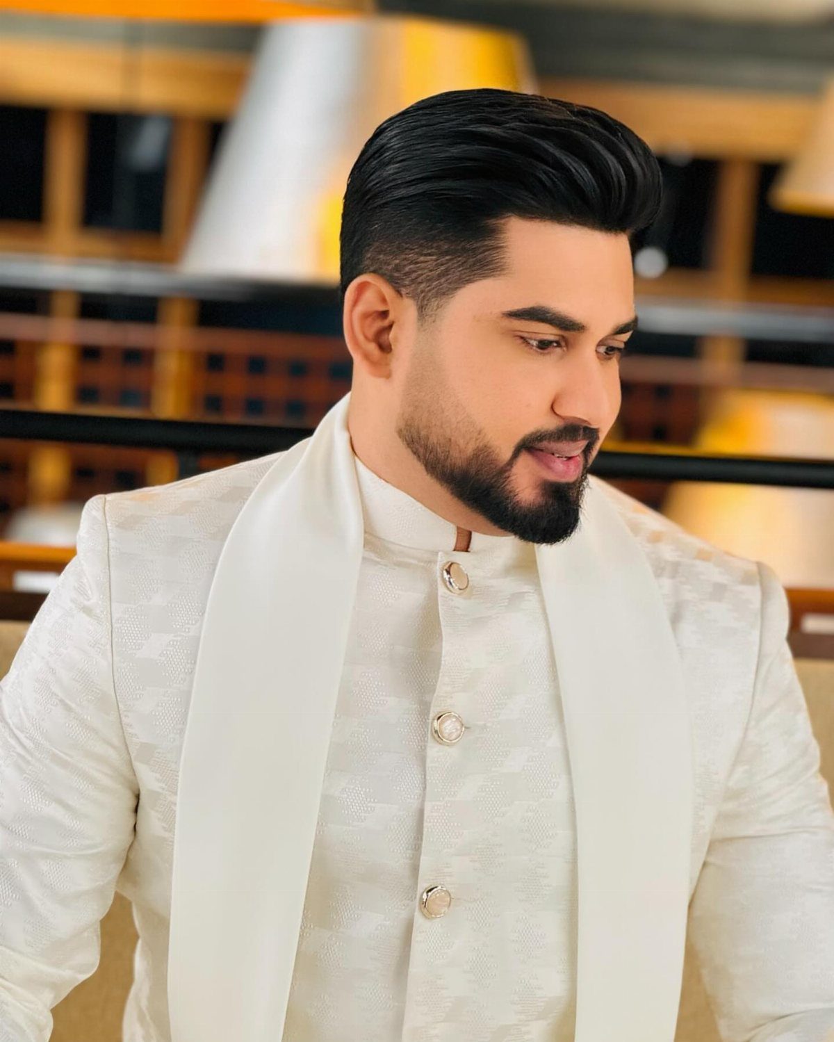 Man with a crisp fade and styled pompadour wearing a white traditional sherwani.