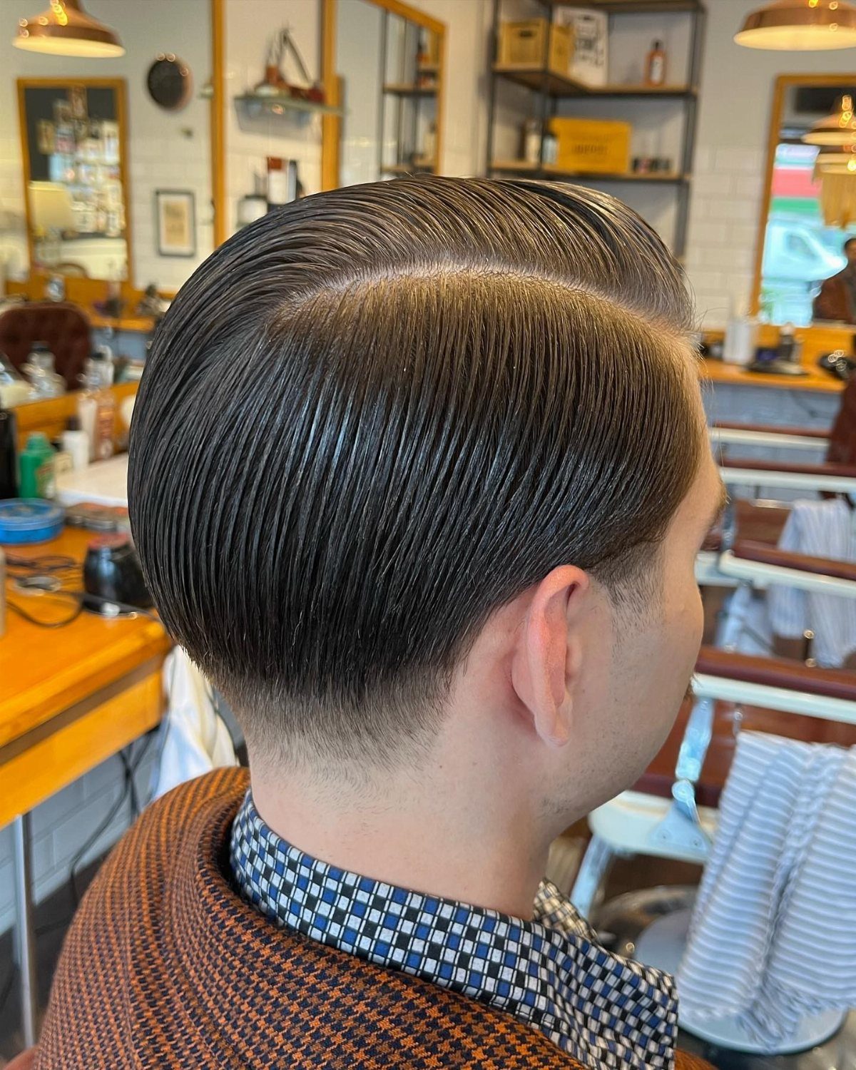 Slicked-back side part hairstyle on a man in a professional barbershop setting.