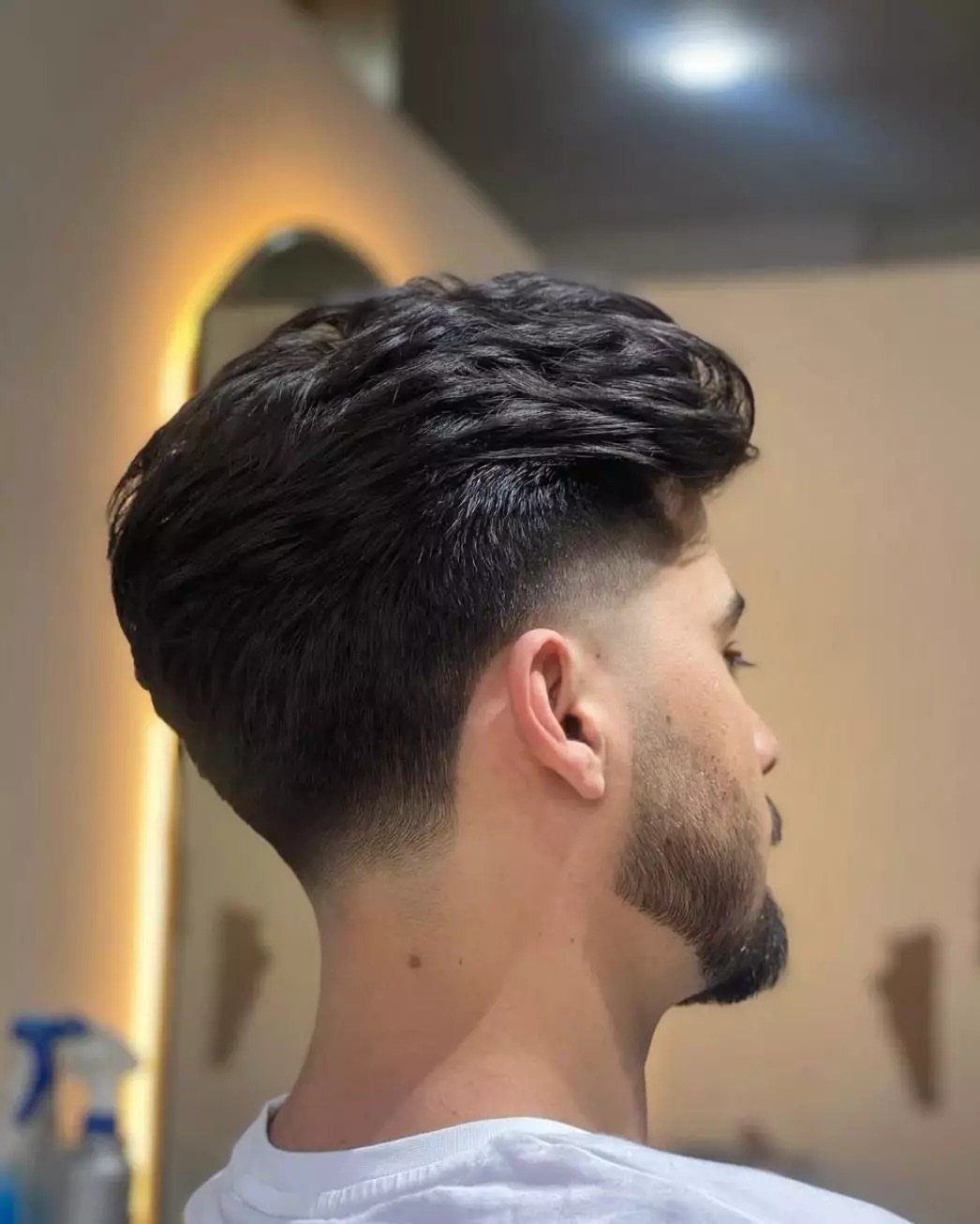 Man with a dark slicked back fade haircut and a groomed beard.