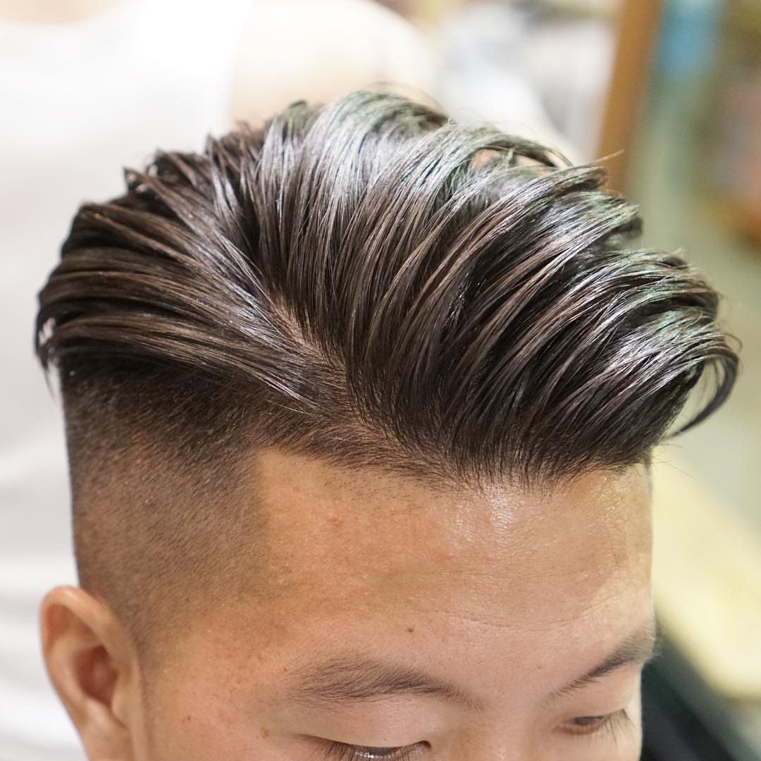 Man with a slicked-back undercut hairstyle and faded sides in a barbershop setting.