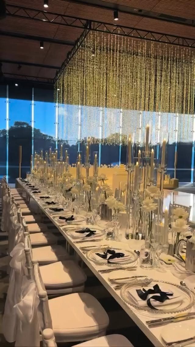 Long white wedding reception table with candles, white flowers, and golden fairy lights.