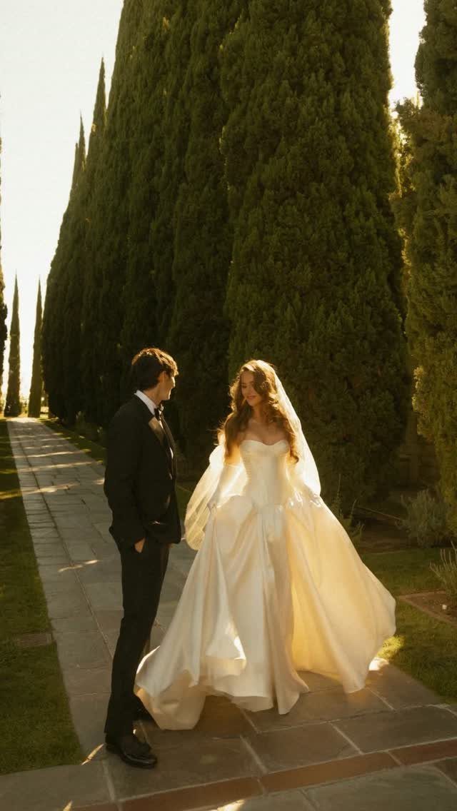 Bride and groom standing on a stone path surrounded by tall cypress trees.