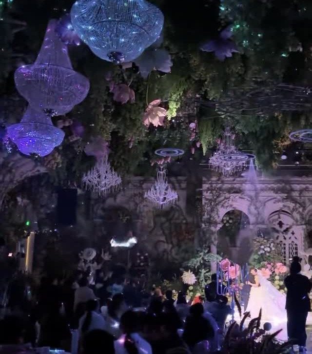 Wedding venue with glowing purple chandeliers, greenery, and a bride in a white gown.