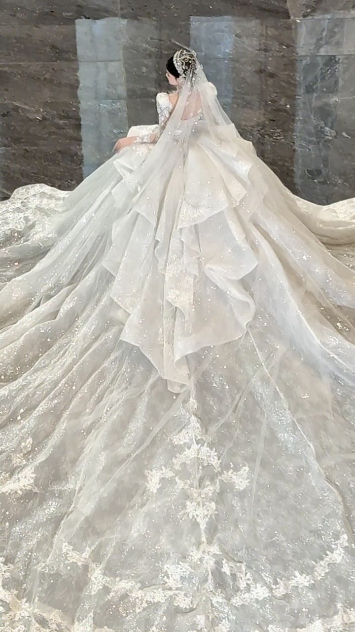 Woman in a voluminous white wedding gown with a long sparkling train and veil.