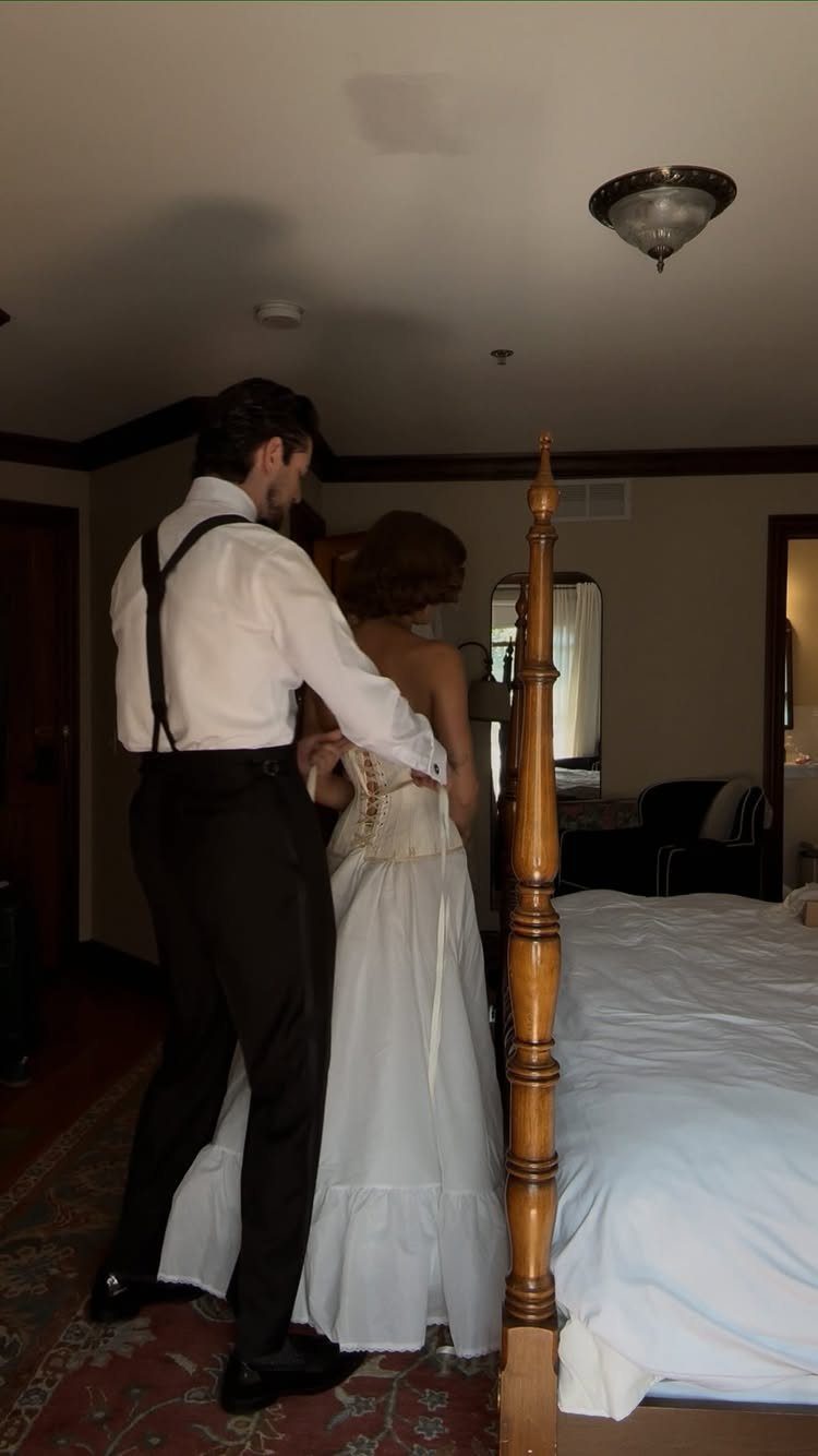 No Wedding Party? 6 Ideas for Celebrating Without One 3 Groom in suspenders helping bride with her white wedding dress in a bedroom
