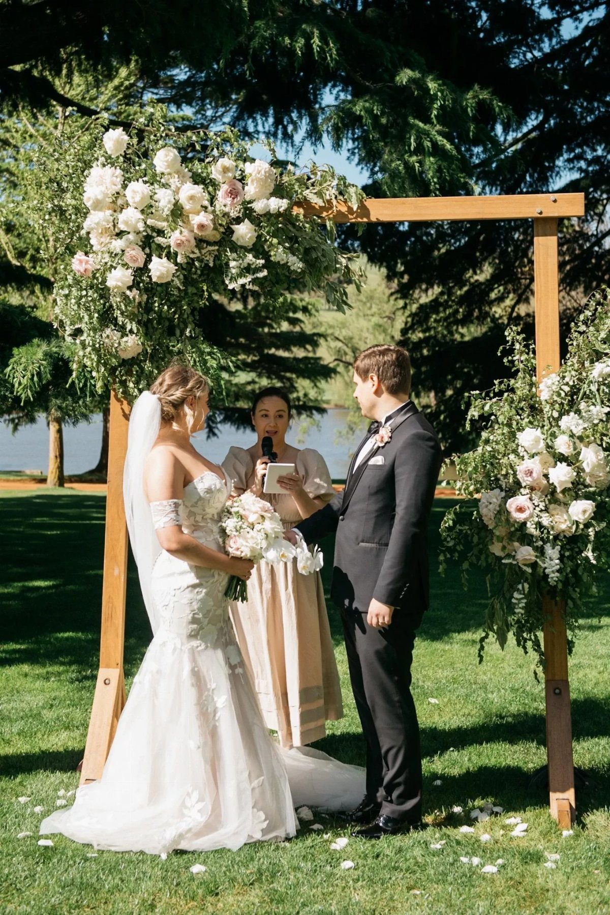 No Wedding Party? 6 Ideas for Celebrating Without One 1 Bride and groom standing under a floral wooden arch during an outdoor wedding ceremony.