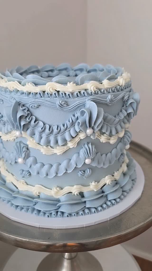 Light blue tiered cake with ornate buttercream ruffles and white pearl decorations.