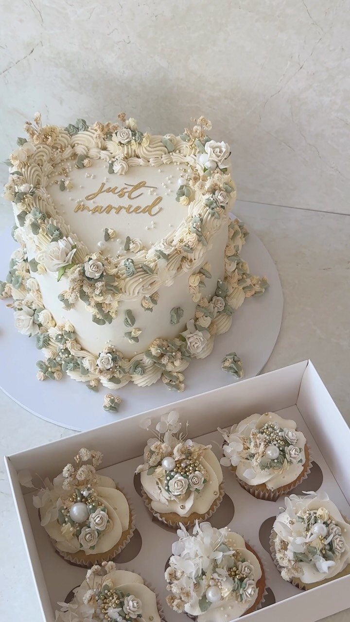 Heart-shaped white wedding cake with floral frosting and matching cupcakes in a box