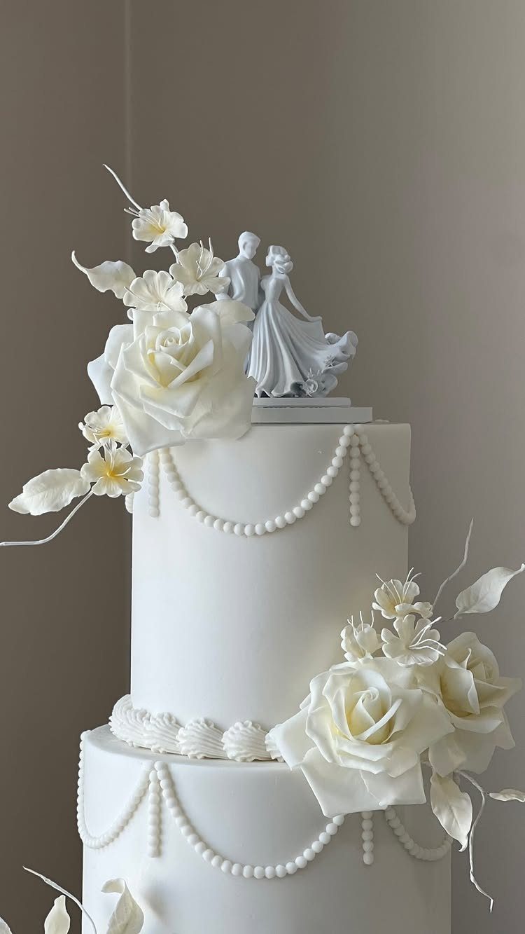 White multi-tiered wedding cake with sugar roses and a bride and groom topper.
