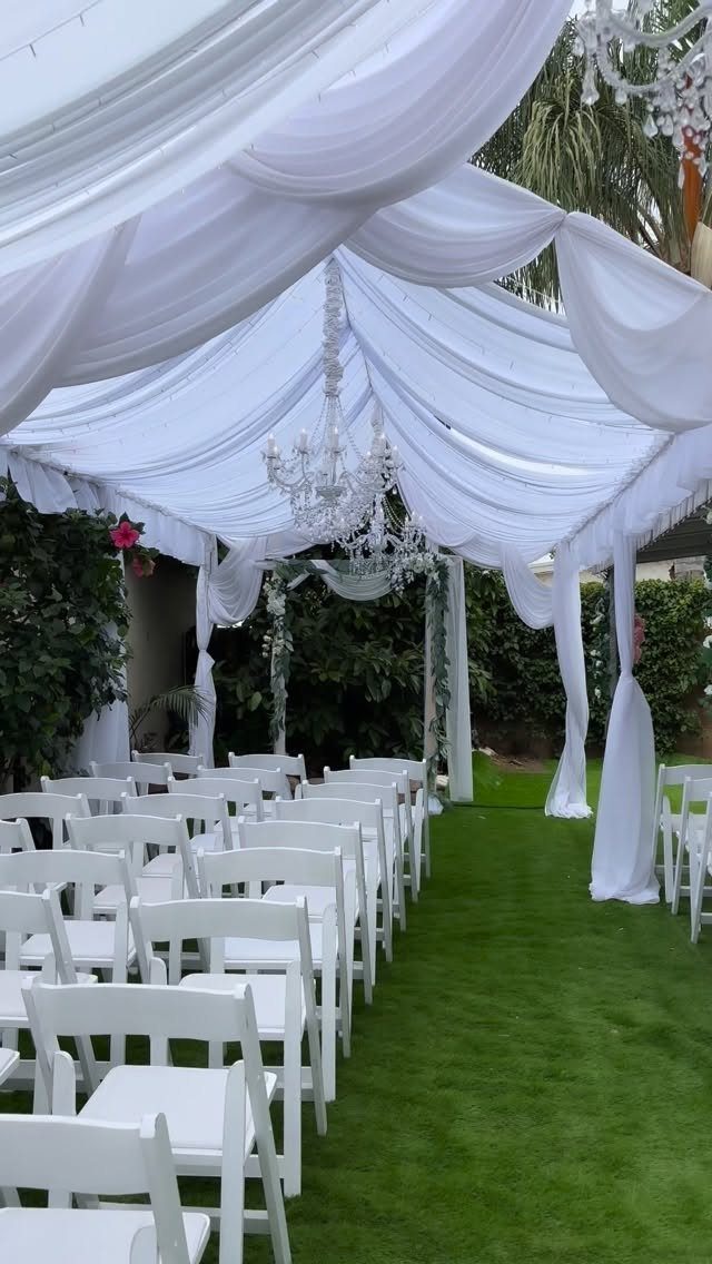 White folding chairs on a green lawn under a draped white fabric canopy.