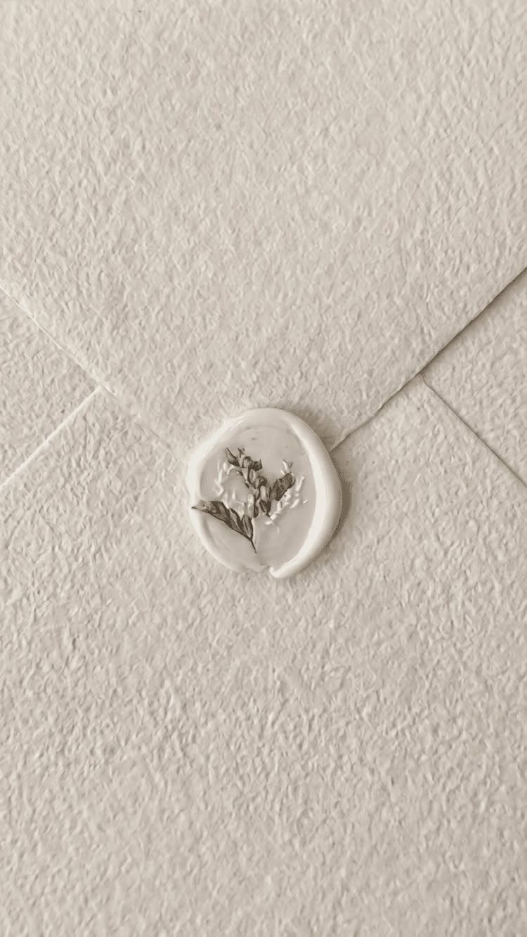 Cream textured paper envelope with a white wax seal and dried greenery.
