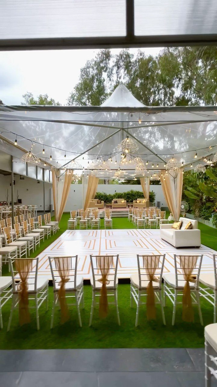 Outdoor wedding ceremony setup with a clear tent, dance floor, and gold chairs.