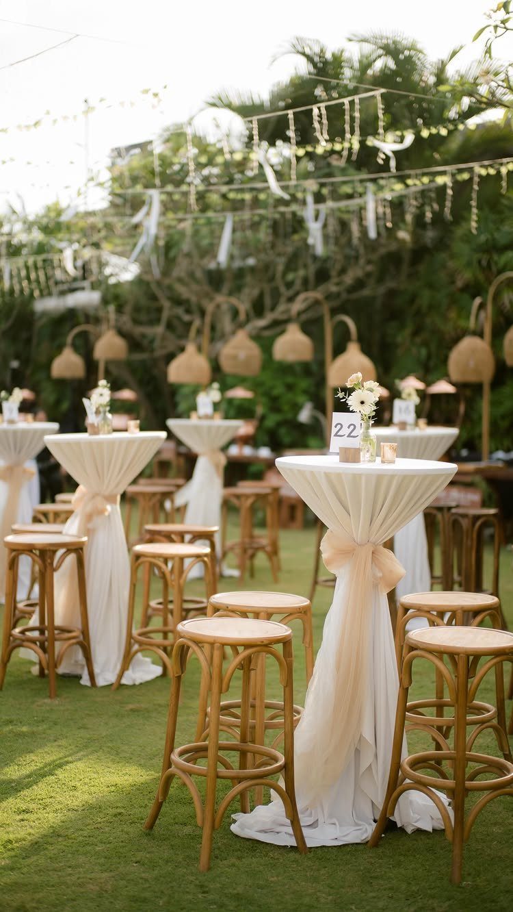 High-top cocktail tables with peach fabric draping and wooden stools on a green lawn
