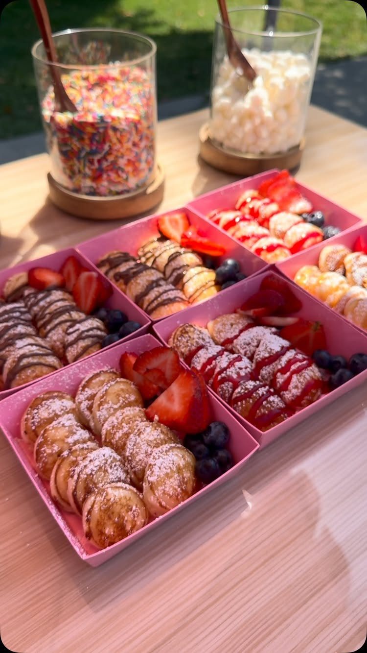Mini pancake boxes with fruit and toppings on a wooden outdoor table.