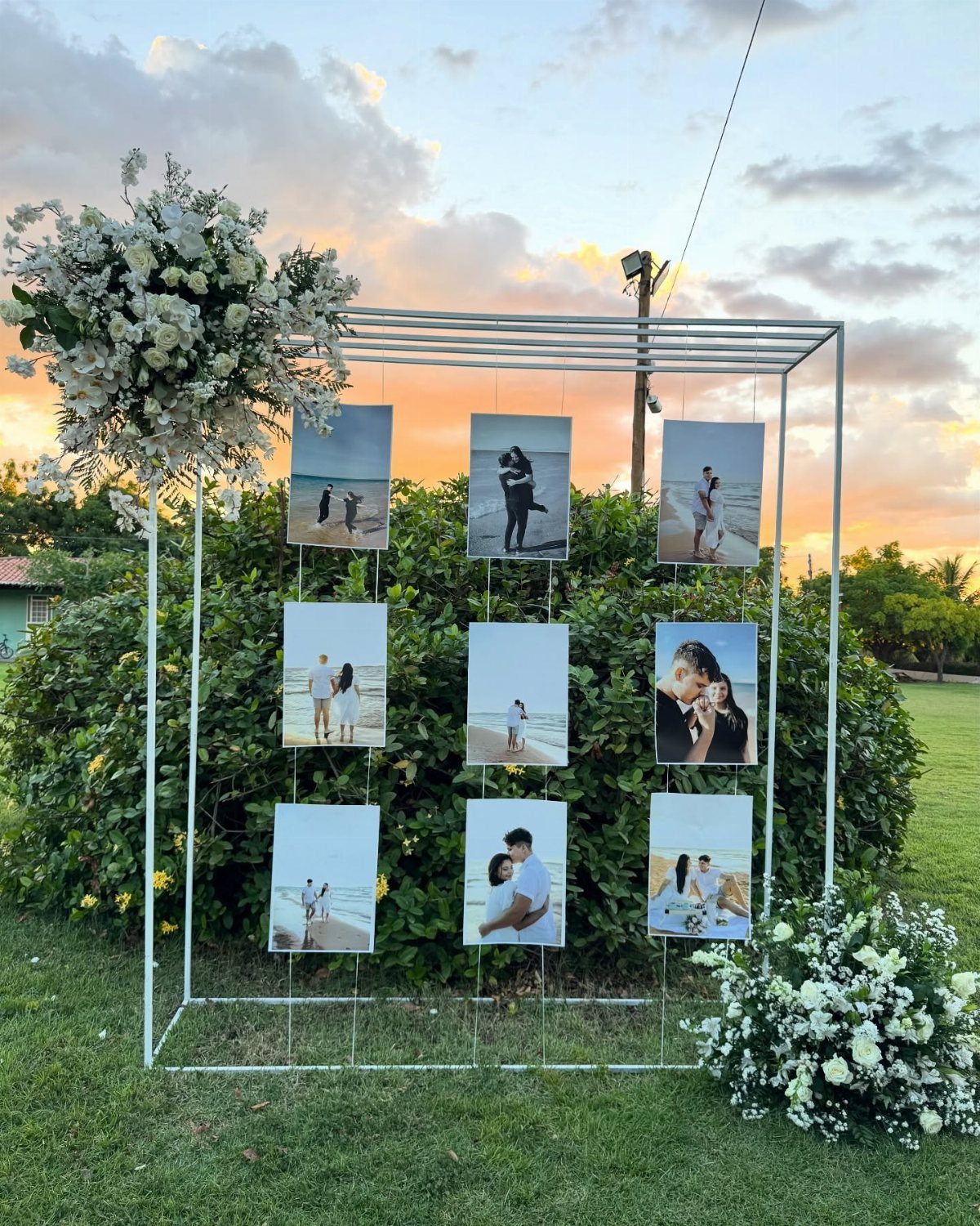 White metal frame with hanging couple photos and white flowers in a garden.