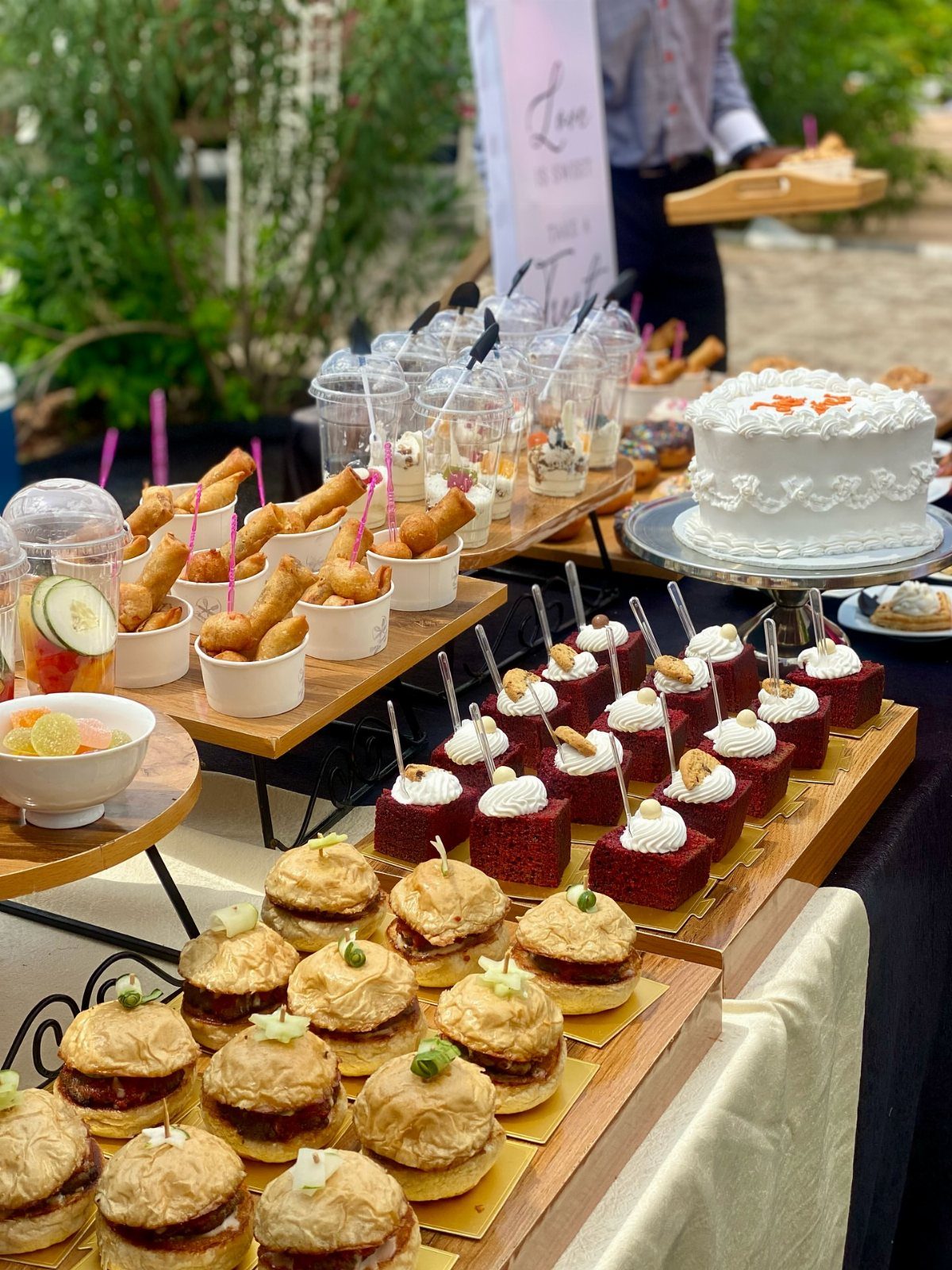 Assorted wedding catering appetizers including sliders and red velvet cakes on wooden platters.