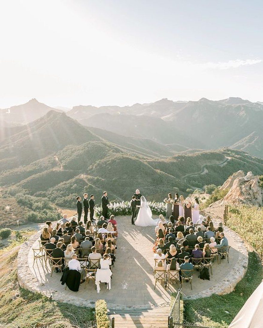 Wedding ceremony on a mountain overlook with guests seated in wooden chairs.