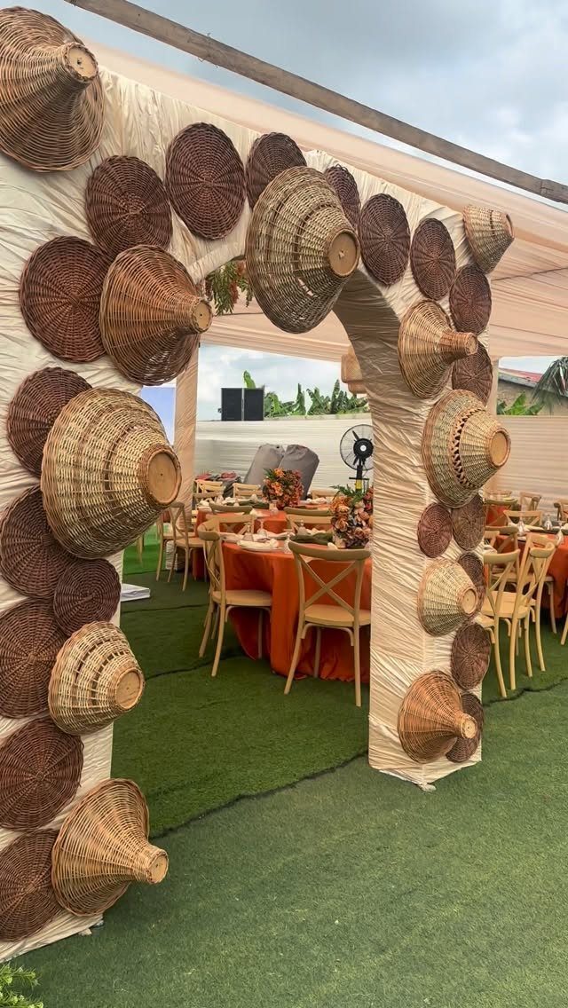 Woven basket decorated archway leading to orange tables at an outdoor wedding event