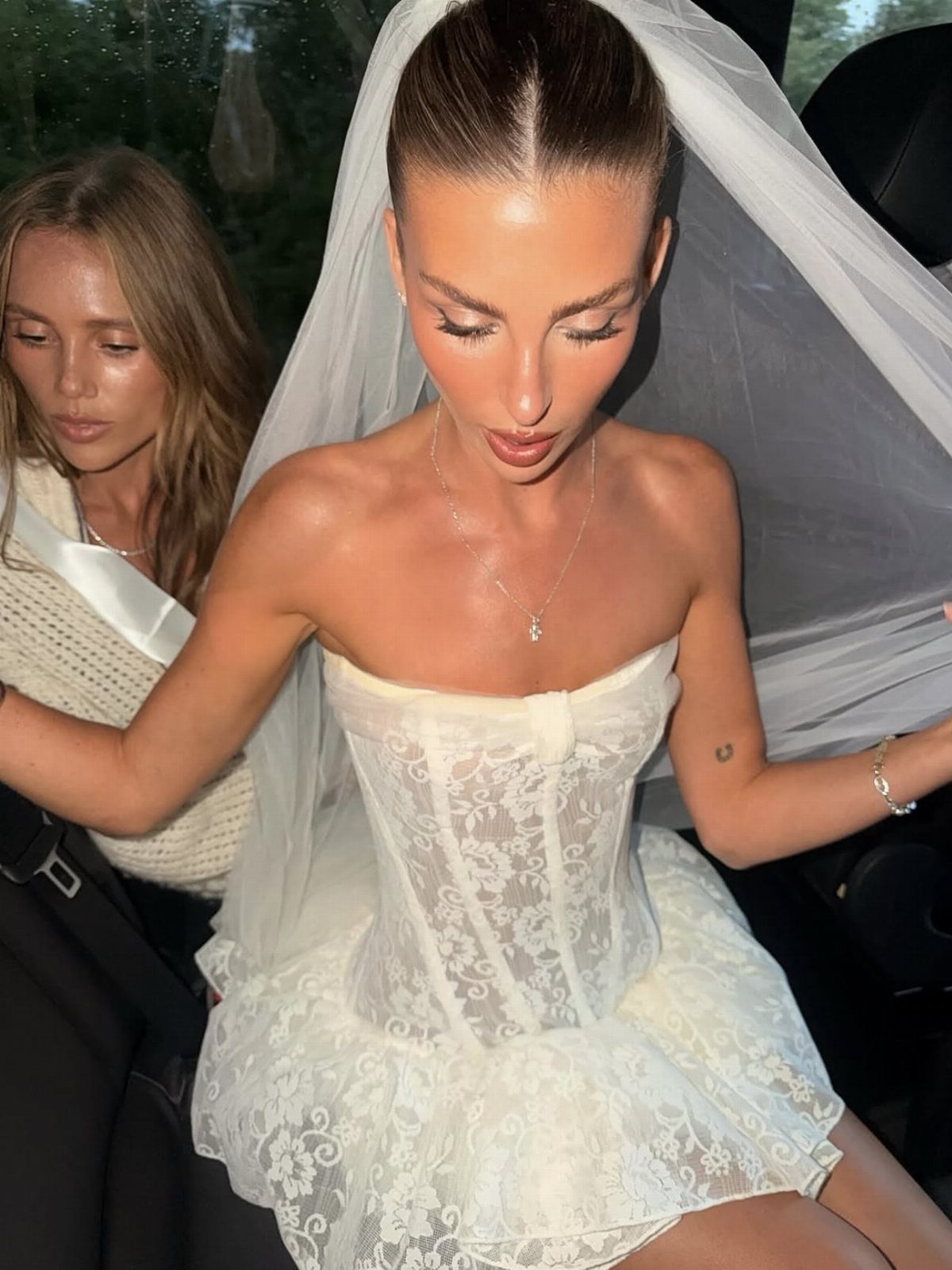 Woman in a white lace strapless minidress and bridal veil sitting in a car.