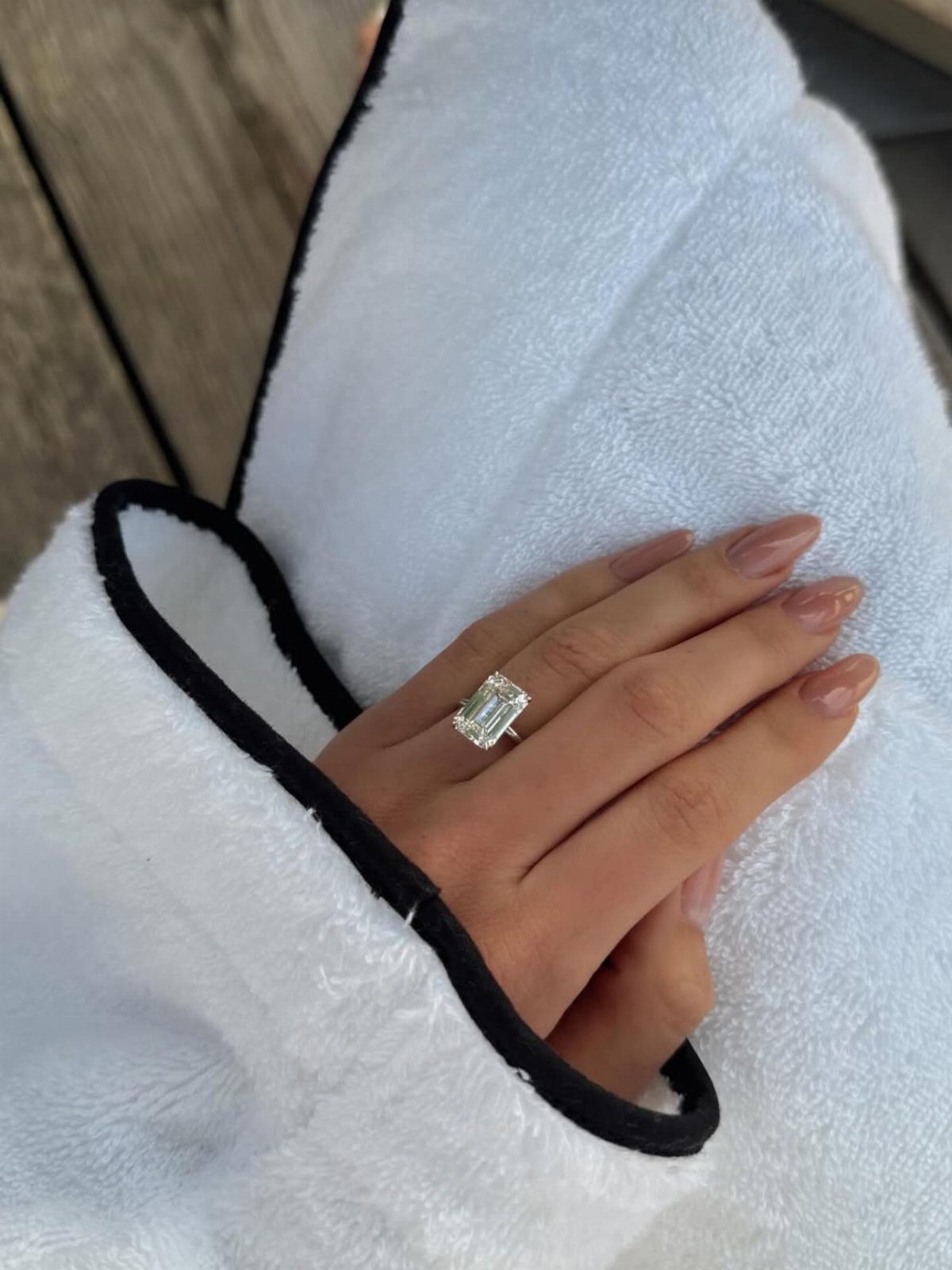Emerald-cut diamond ring on a hand resting against a white robe with black trim.