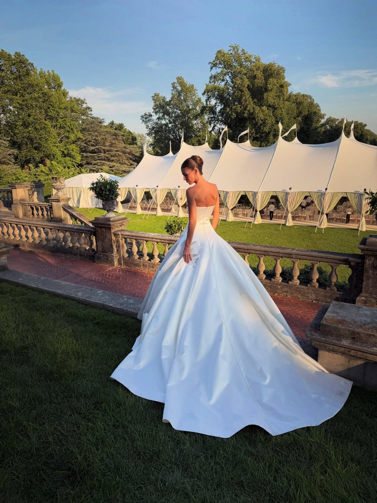 Woman in a white strapless wedding gown posing on a stone terrace near a tent.