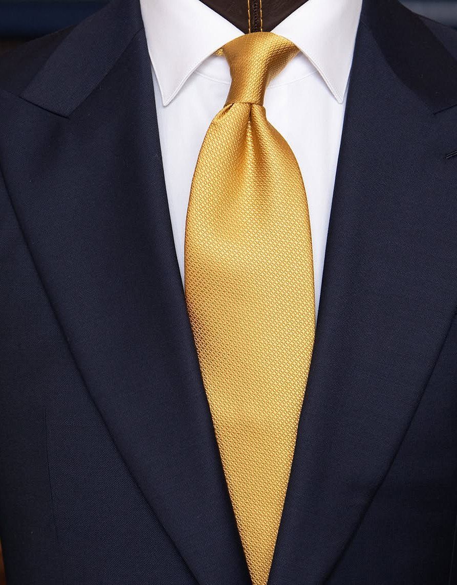 Gold silk necktie paired with a white shirt and navy blue suit jacket.