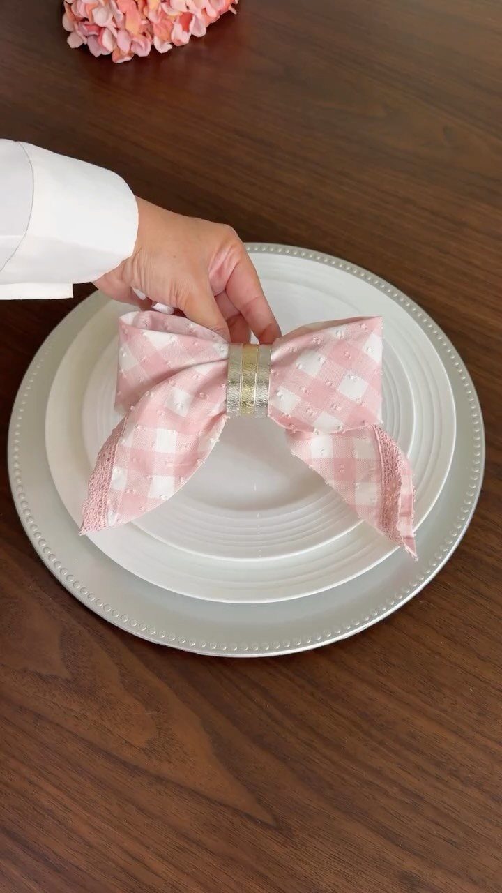 Pink checkered napkin folded into a bow on white plates on wooden table.