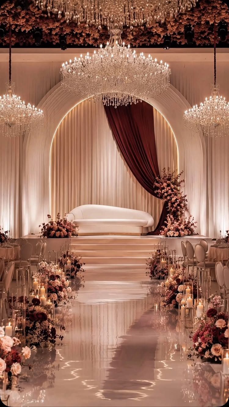 Opulent wedding venue with deep red and blush pink floral arrangements and crystal chandeliers.