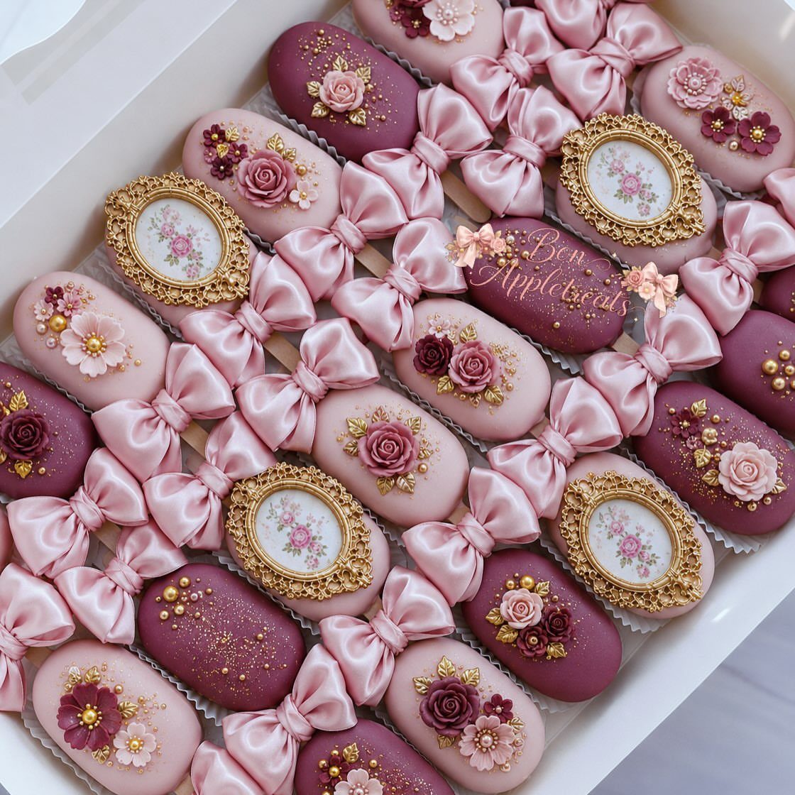 Pink and mauve oval candies decorated with frosting roses, gold frames, and satin bows.
