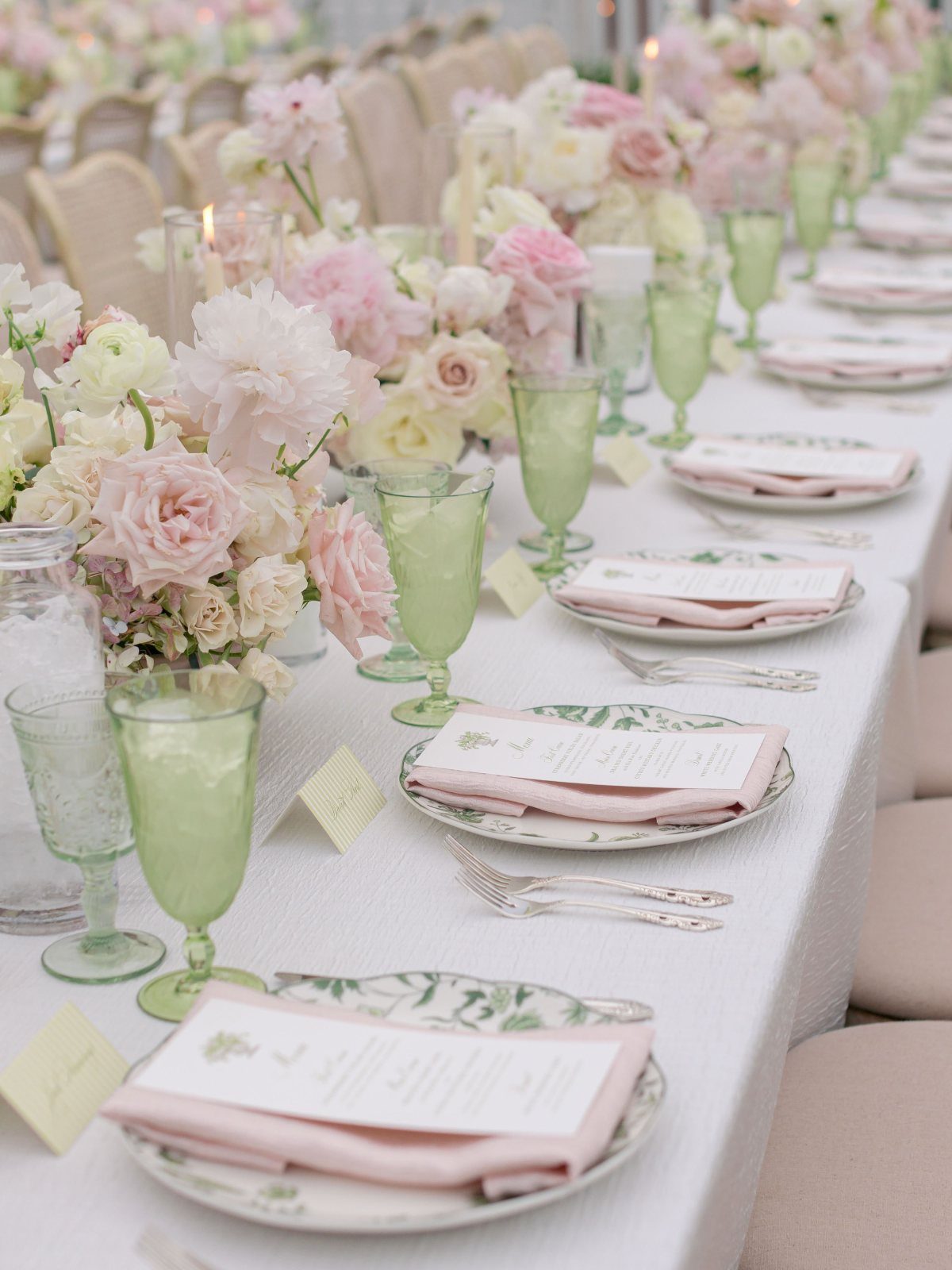 Wedding table setting with pink flowers, green glasses, and pink napkins on white linens