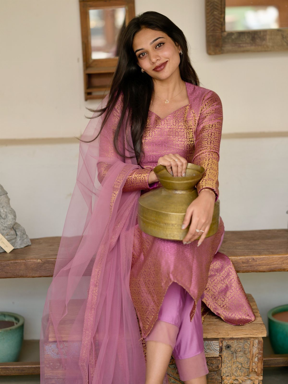 12 Pre Wedding Photoshoot Outfit Ideas for Couples 8 Woman in mauve traditional Indian outfit with gold embroidery holding a gold pot.