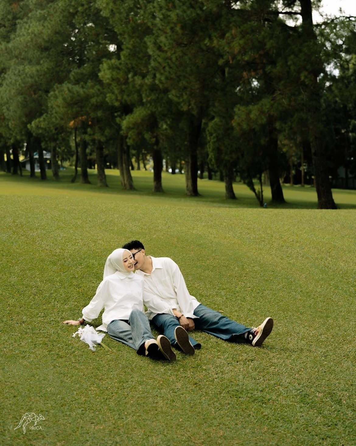 12 Pre Wedding Photoshoot Outfit Ideas for Couples 10 Couple in white shirts and blue jeans sitting on a green grassy field.