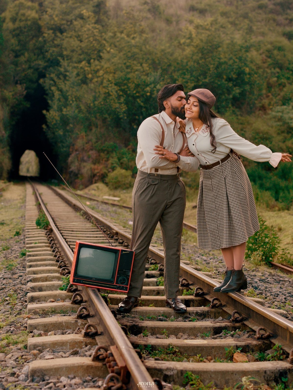 12 Pre Wedding Photoshoot Outfit Ideas for Couples 7 Couple posing on railroad tracks, woman wearing a white lace blouse and checkered skirt.