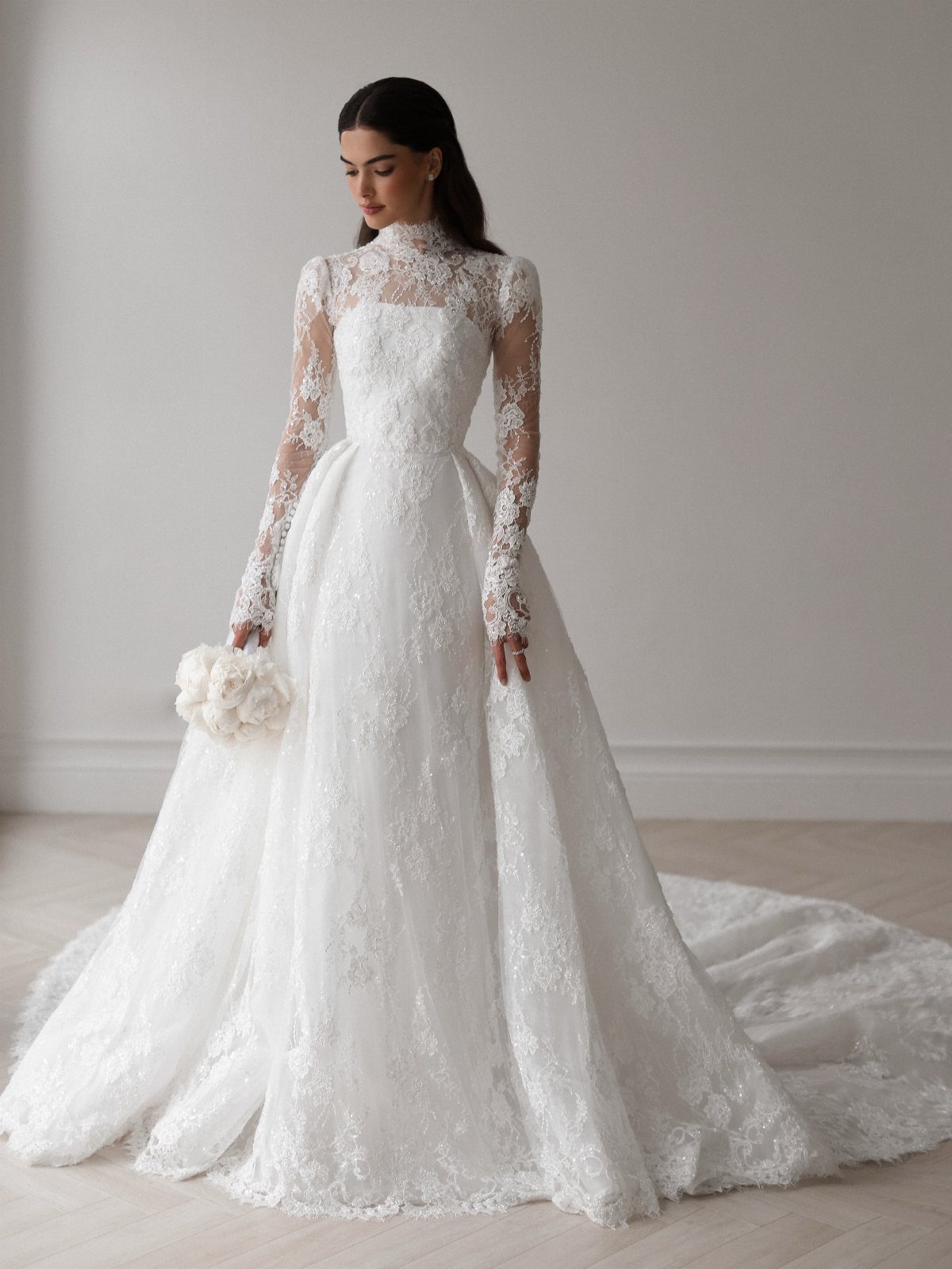 Woman in a white lace A-line wedding dress with long sleeves and high neck.
