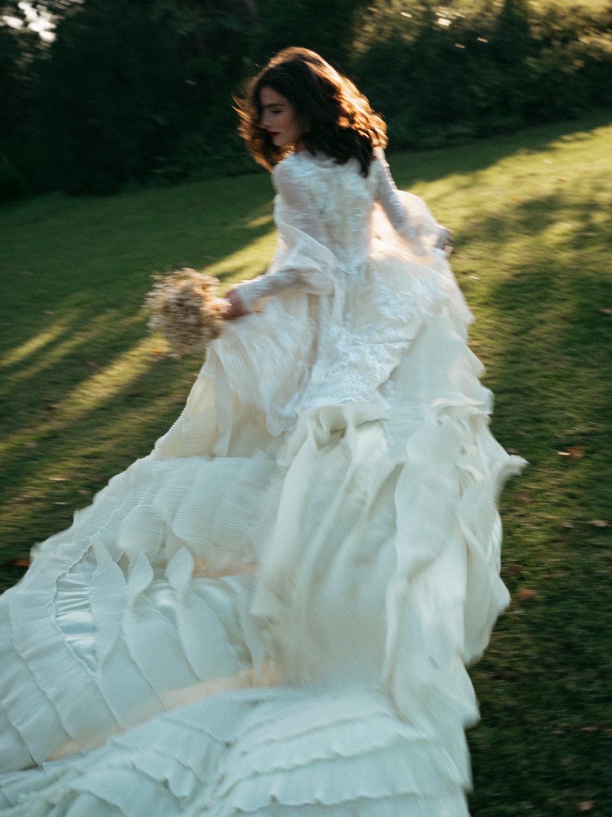 Woman in a voluminous white ruffled wedding dress walking through a sunny green field