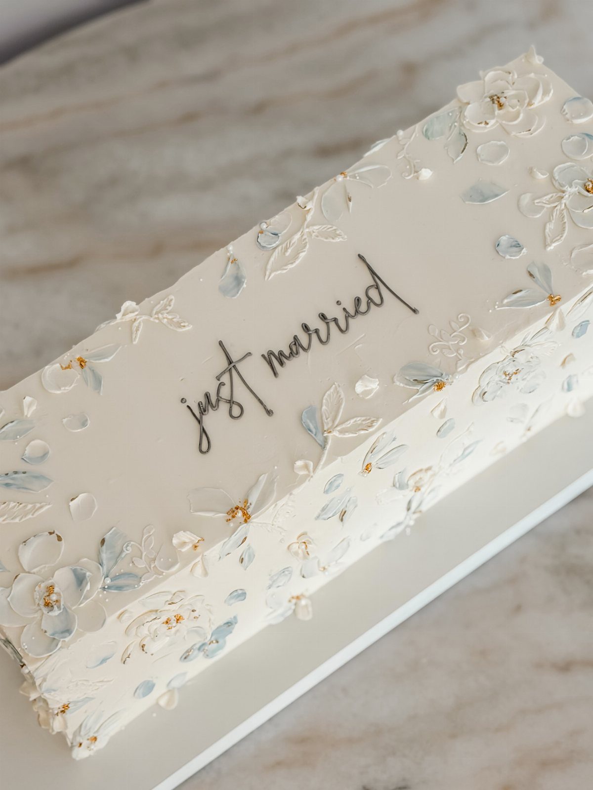 Rectangular white wedding cake with buttercream flowers and just married script